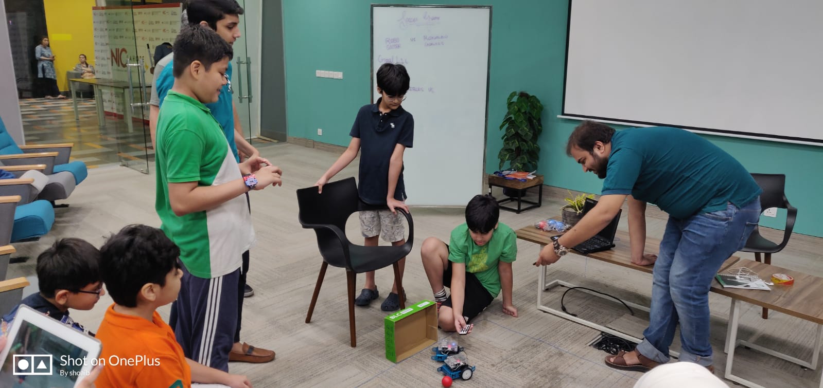 A child driving a small robot with a wireless remote while classmates watch the robot move across the floor
