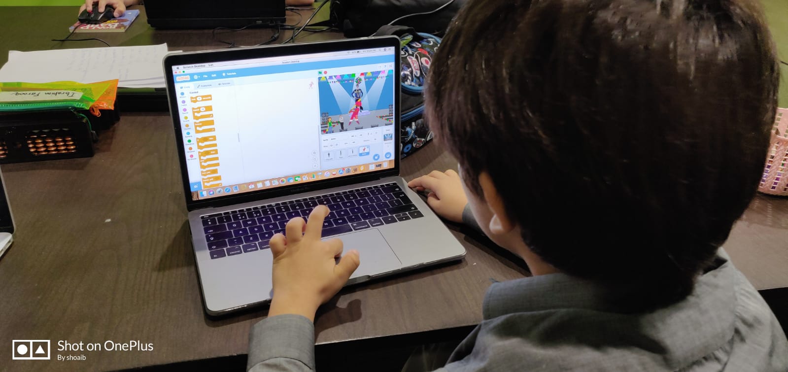 A child building a game in Scratch on a laptop, viewed over their shoulder